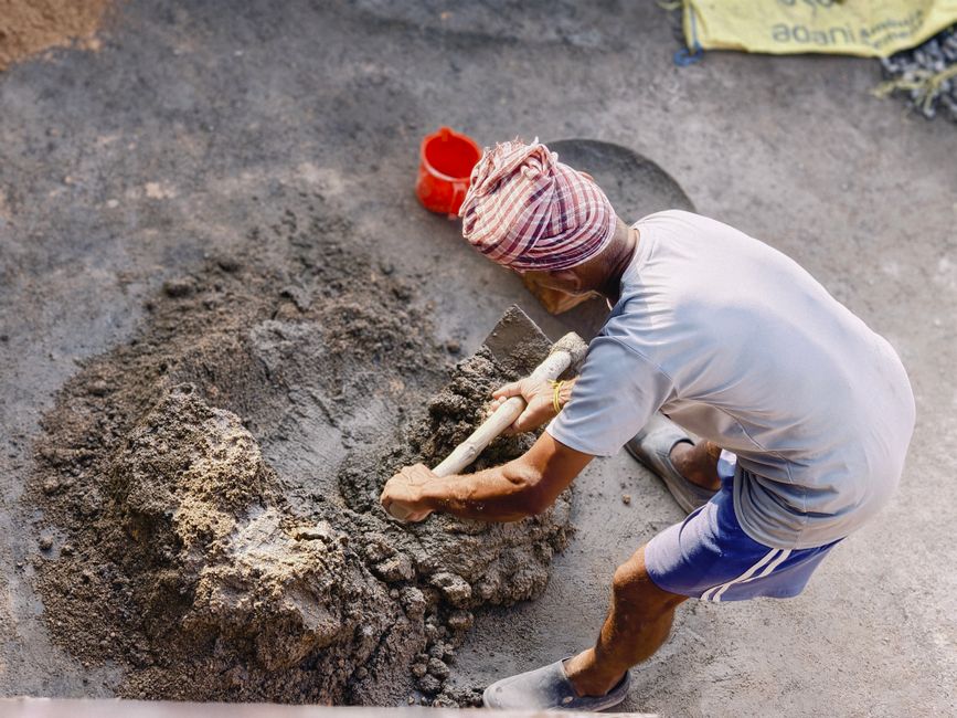 A construction worker mixing cement outdoors, showcasing manual labor and building preparation.